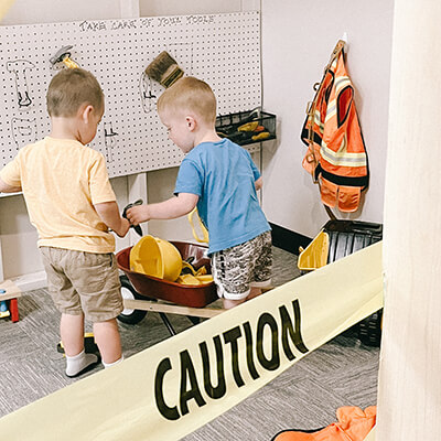 Two boys playing with tools behind construction tape